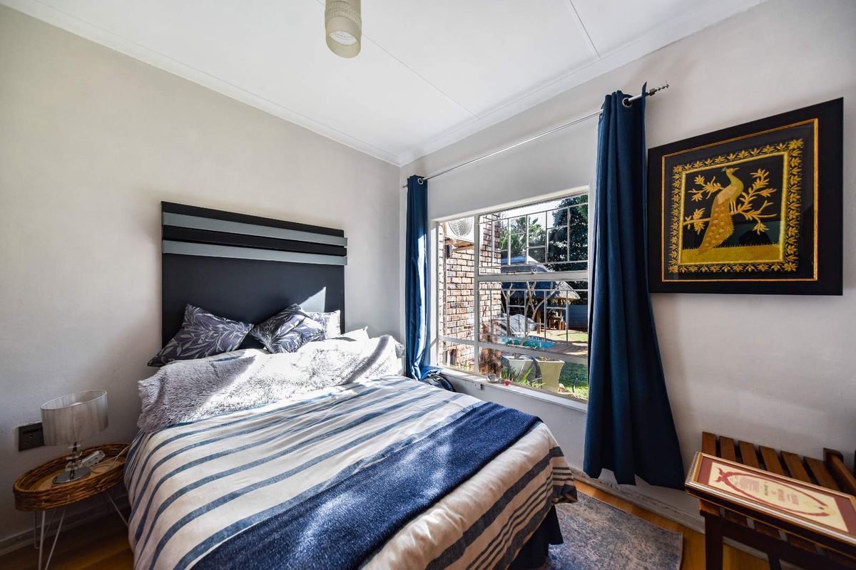 A well-lit bedroom featuring hardwood flooring, a large window with security bars, and neutral wall finishes.