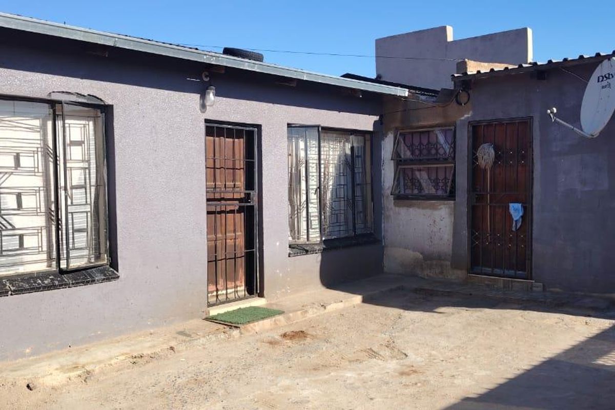 Rear exterior view of the property featuring a concrete courtyard, security gates, and window bars on the building facade.