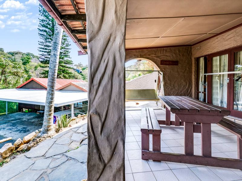 A covered outdoor patio featuring tiled flooring, a unique textured pillar, and direct access to the garden area.