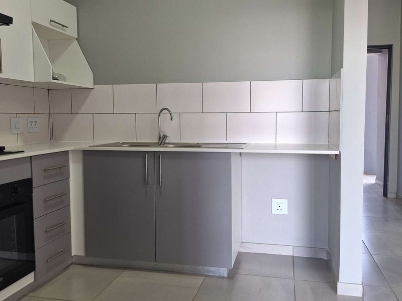 A clean, modern kitchen featuring grey and white cabinetry, a built-in oven with gas hob, tiled backsplash, and neutral floor tiles.