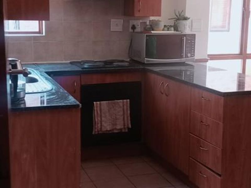 A functional kitchen featuring wooden cabinetry, granite countertops, built-in oven and hob, and tiled flooring with a neutral backsplash.