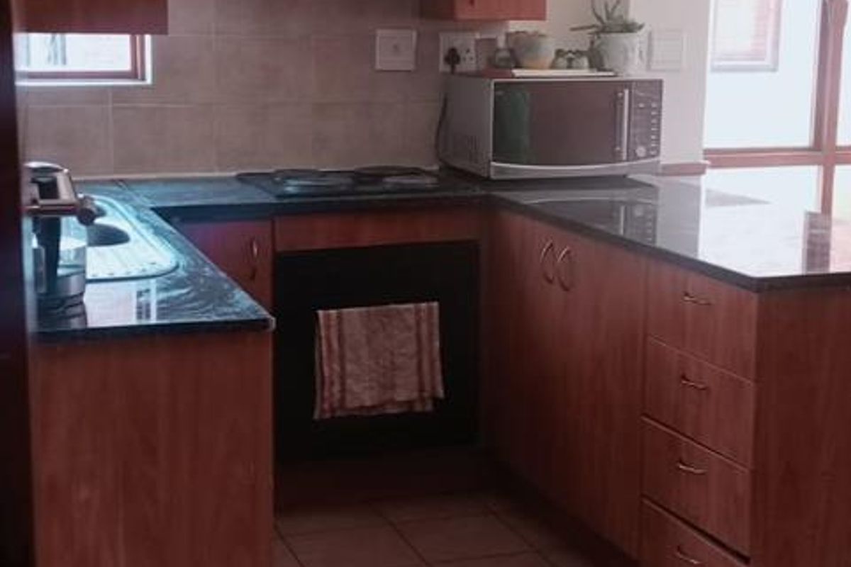 A functional kitchen featuring wooden cabinetry, granite countertops, built-in oven and hob, and tiled flooring with a neutral backsplash.