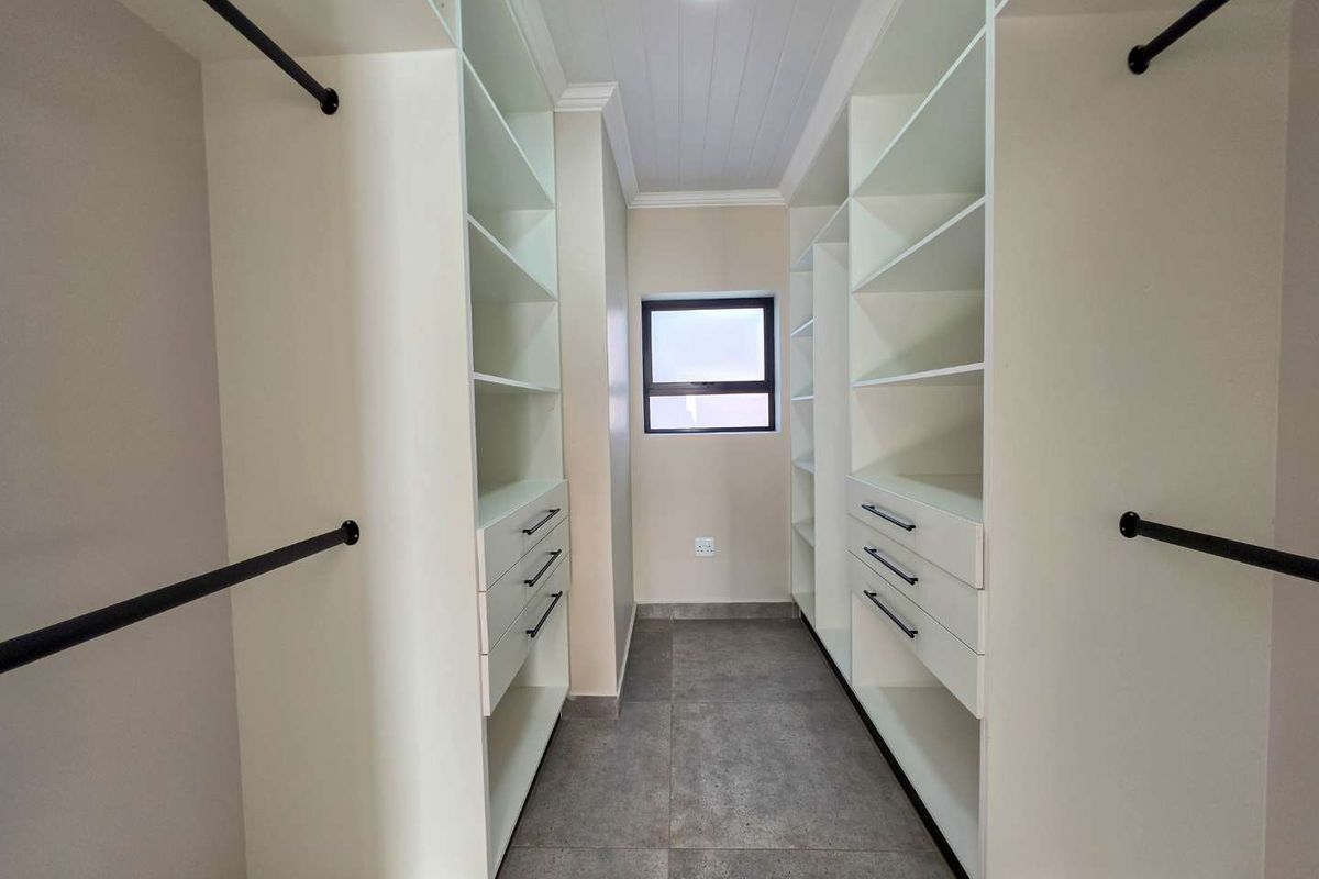 A modern, empty walk-in closet featuring extensive built-in cabinetry, drawers, hanging rails, and neutral tiled flooring.