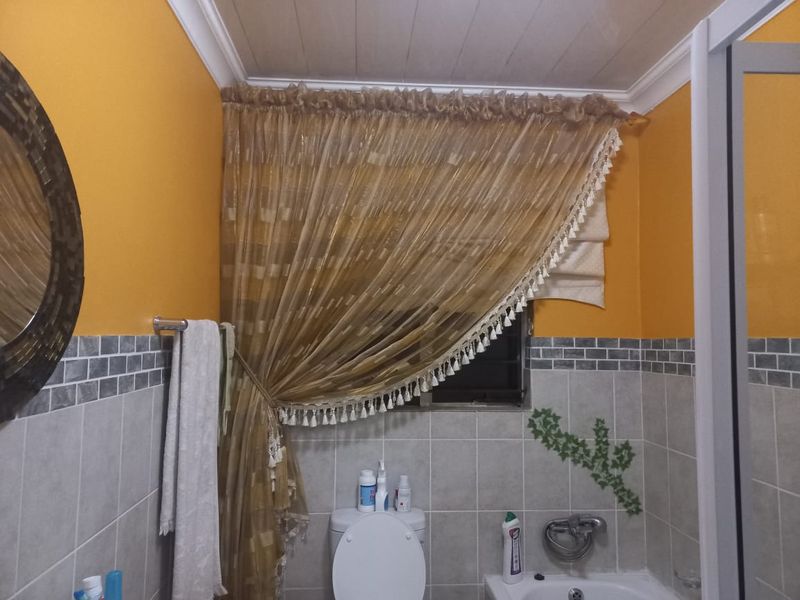 A bathroom featuring tiled walls with a decorative border, a toilet, and a bathtub with a mixer tap.