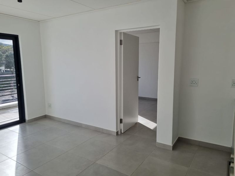 A bright, empty living area featuring neutral tiled flooring, clean white walls, and a sliding glass door providing access to an outdoor space.