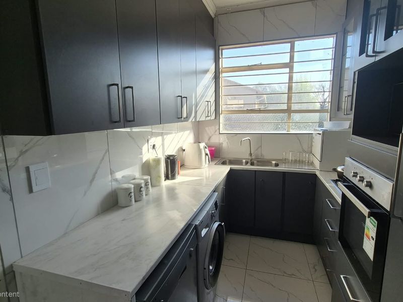 Modern kitchen featuring dark cabinetry, marble-look countertops, tiled backsplash, built-in oven, and a double sink with window views.