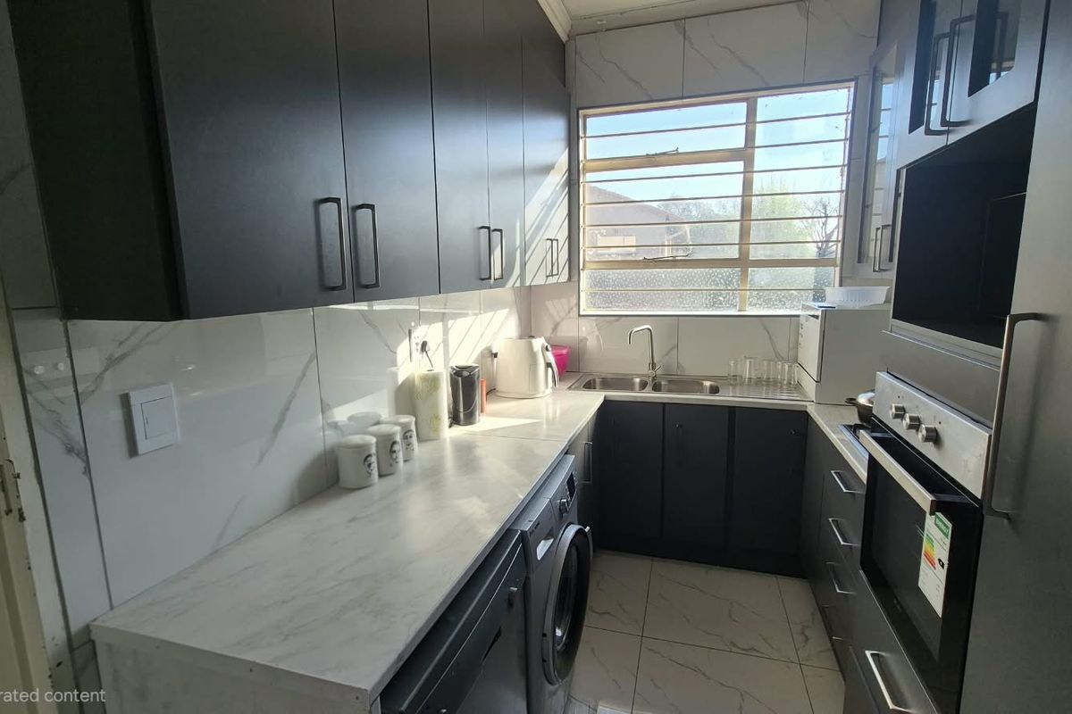 Modern kitchen featuring dark cabinetry, marble-look countertops, tiled backsplash, built-in oven, and a double sink with window views.