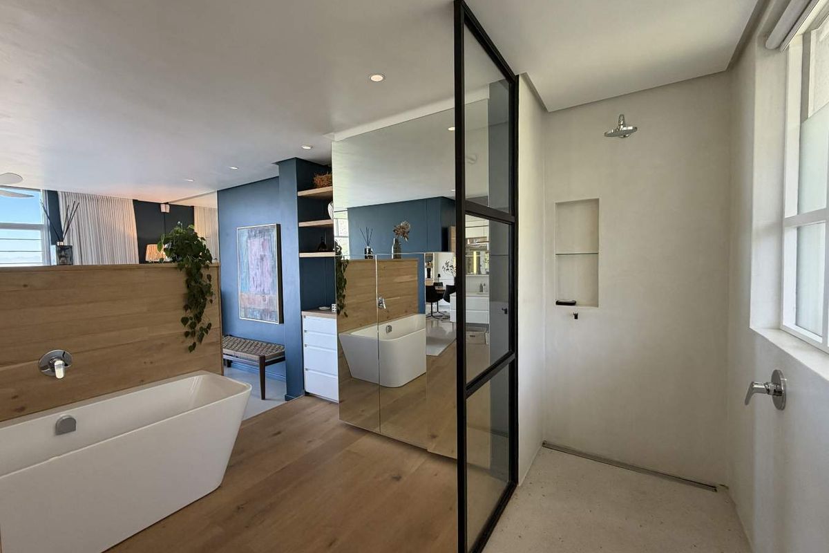 Modern open-plan bathroom featuring a freestanding bathtub, walk-in shower with a black-framed glass partition, and integrated shelving.