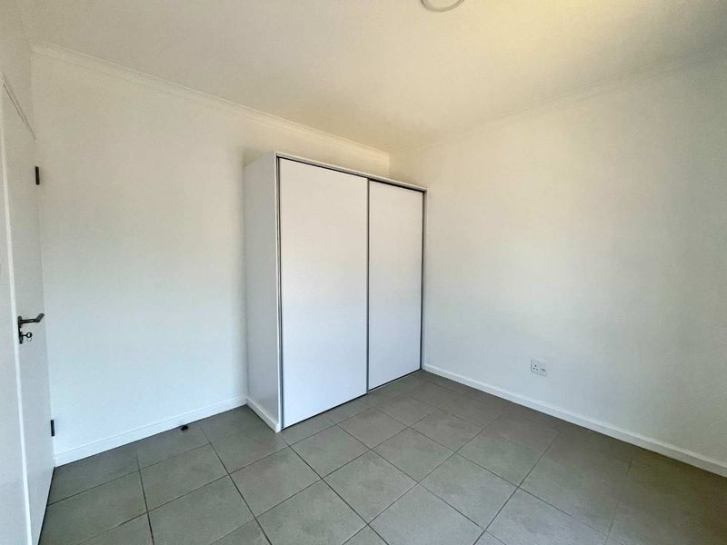 A clean, empty bedroom featuring neutral tiled flooring and a modern white built-in wardrobe with sliding doors.