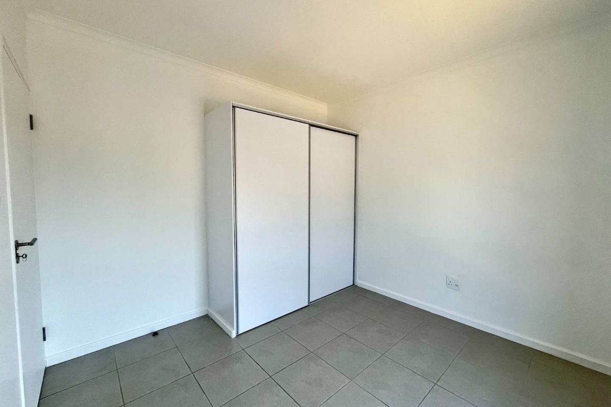 A clean, empty bedroom featuring neutral tiled flooring and a modern white built-in wardrobe with sliding doors.