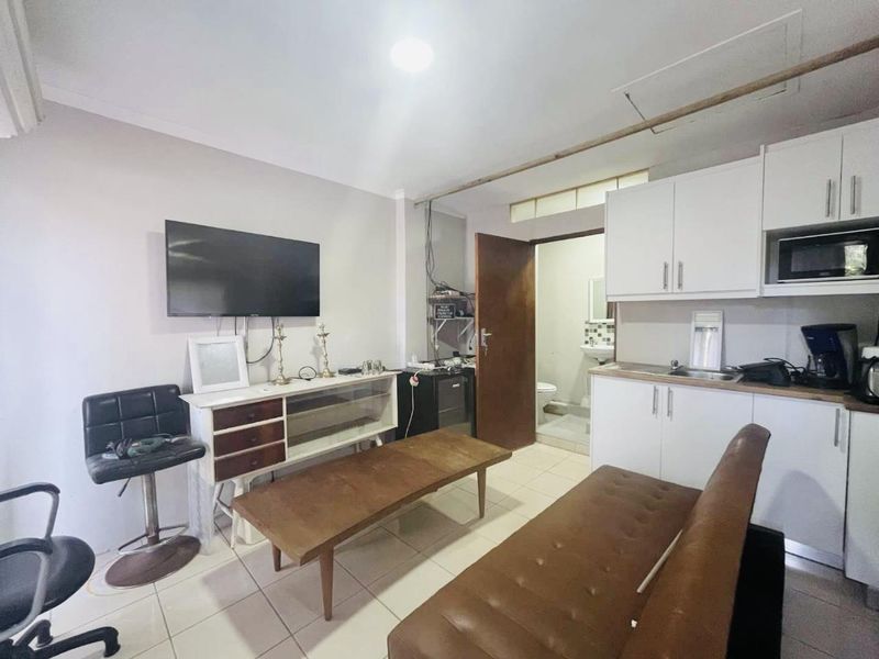 Compact open-plan living area featuring a kitchenette with built-in cabinetry and tiled flooring, leading to an adjacent bathroom.