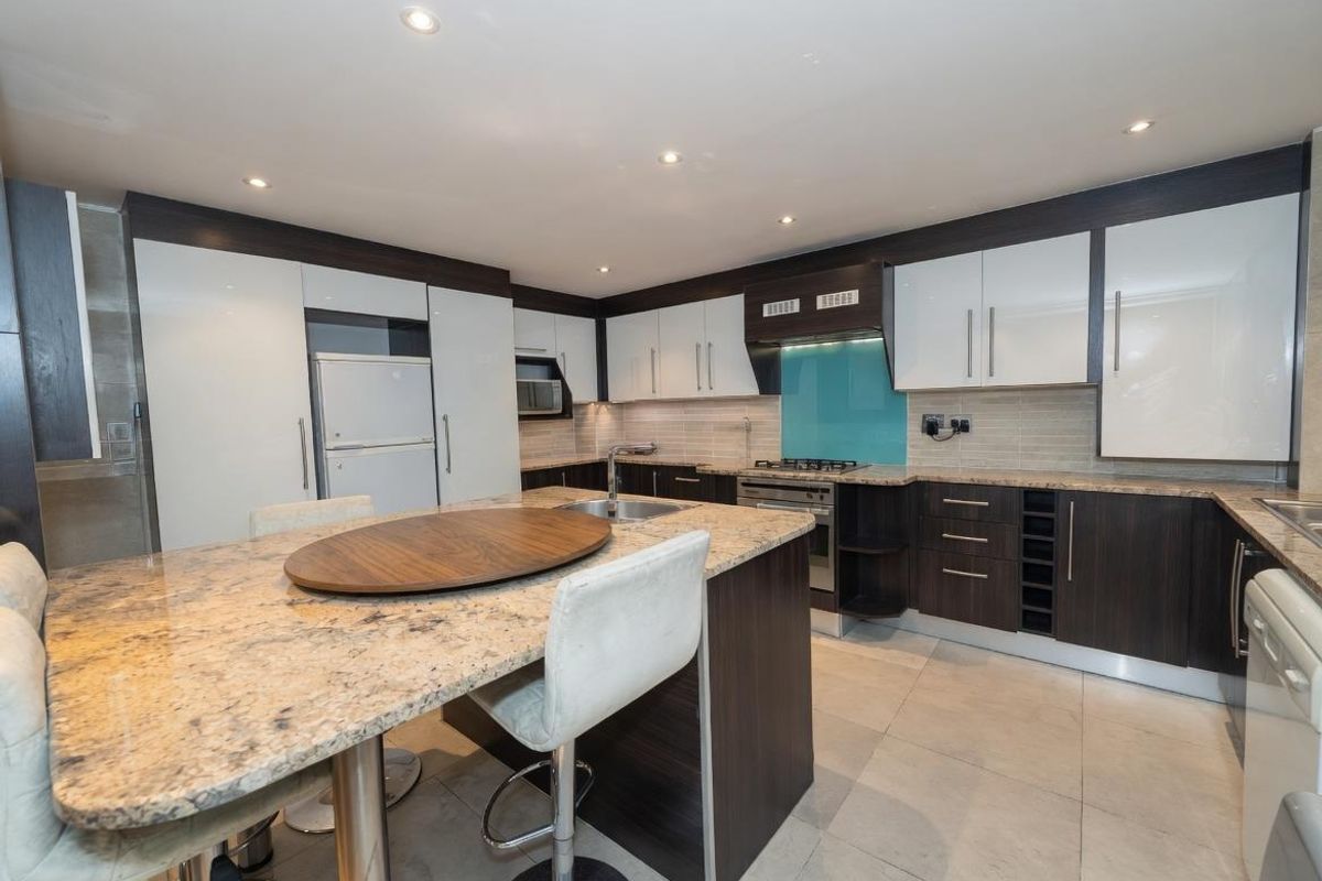 Modern kitchen featuring granite countertops, a central island with breakfast bar, high-gloss cabinetry, and integrated stainless steel appliances.