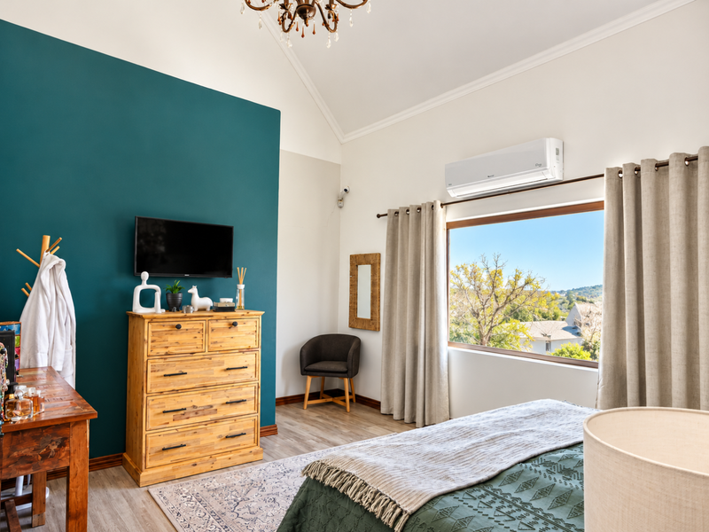 A bright bedroom featuring a vaulted ceiling, split-system air conditioning, and a large window with scenic views.