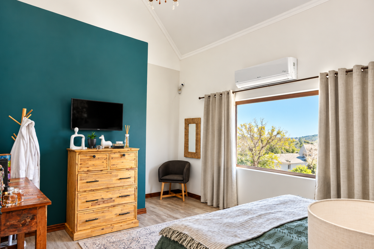 A bright bedroom featuring a vaulted ceiling, split-system air conditioning, and a large window with scenic views.