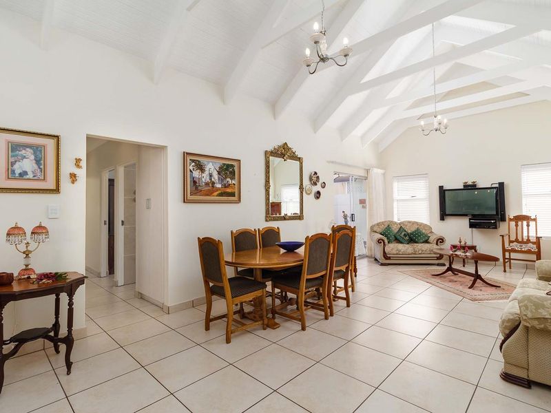 Spacious open-plan living and dining area featuring high vaulted ceilings with exposed beams, ceramic tiled flooring, and direct access to the outdoor patio.