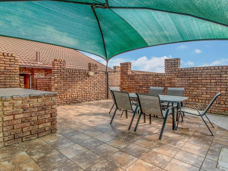 Outdoor patio area featuring a built-in brick braai, tiled flooring, and a protective shade sail, enclosed by brick boundary walls.