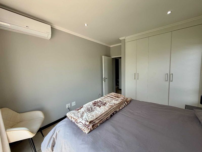 A well-maintained bedroom featuring neutral wall tones, built-in storage cupboards, and a wall-mounted air conditioning unit.