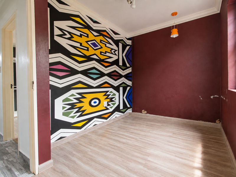 An empty bedroom featuring laminate flooring, a decorative mural wall, and a window with security bars, requiring minor cosmetic repairs to the wall finishes.