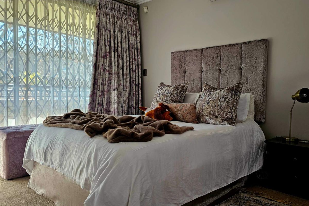 A comfortable bedroom featuring a large window with security gate and curtains, providing natural light and access to the exterior.