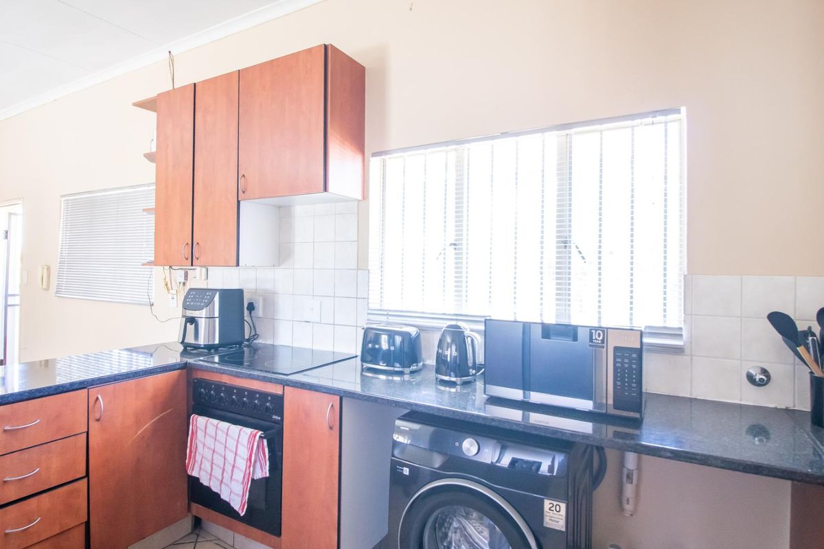 Functional kitchen featuring wood-look cabinetry, dark laminate countertops, integrated oven, hob, and dedicated space for laundry appliances under the counter.