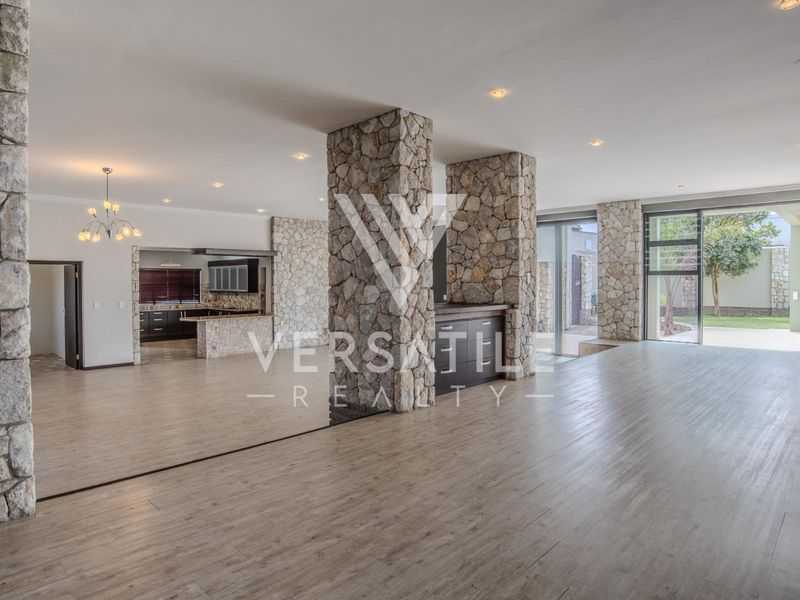 Spacious open-plan living area featuring striking stone-clad columns, modern laminate flooring, and seamless flow to the outdoor patio through large sliding glass doors.