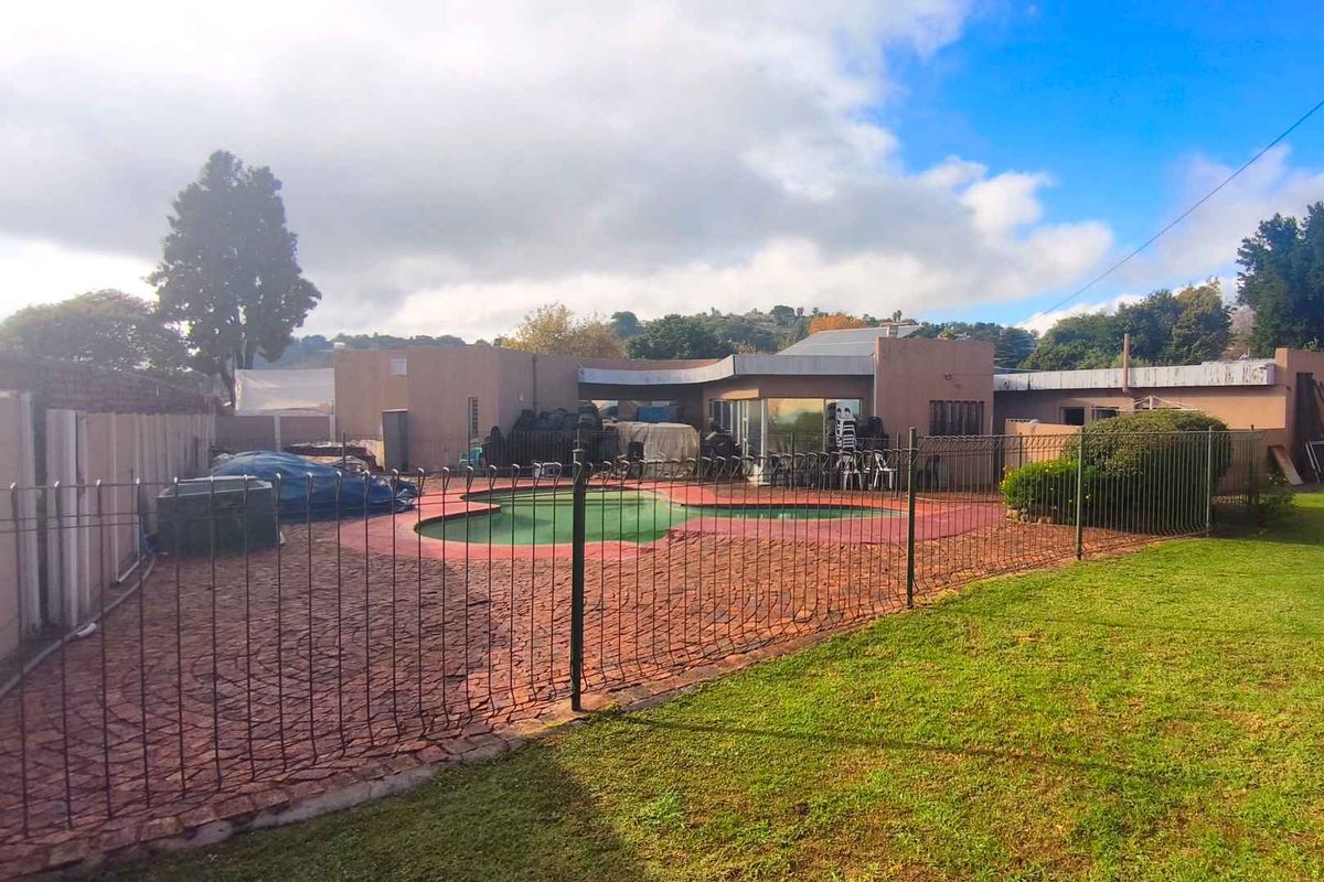 Rear view of the property featuring a swimming pool, paved patio area, and surrounding garden space enclosed by metal fencing.