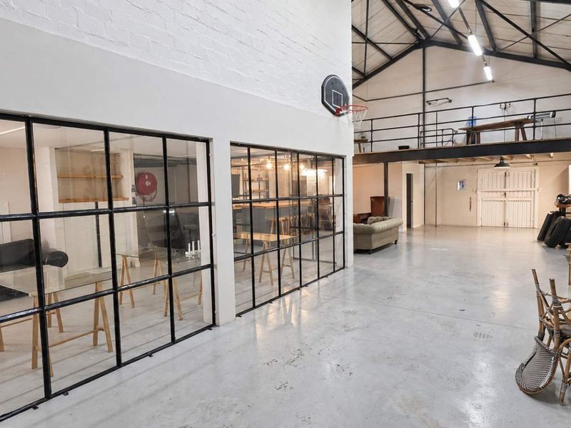 Spacious industrial open-plan area featuring high ceilings with exposed trusses, polished concrete floors, and modern steel-framed glass partitions creating distinct zones.