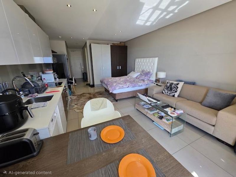 An open-plan studio apartment featuring a modern kitchen with white cabinetry, tiled flooring, and a combined living and sleeping area.