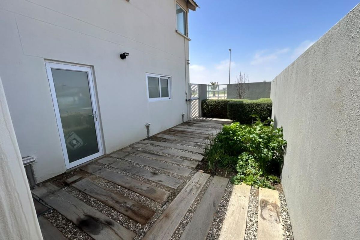 A rear exterior area featuring a timber sleeper pathway set in gravel, enclosed by a boundary wall with a security gate.