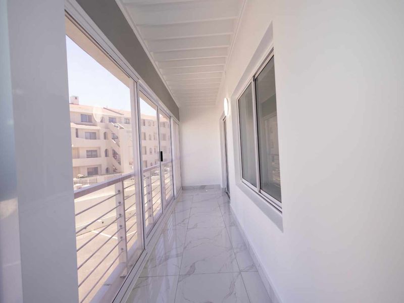 A bright, modern enclosed balcony featuring sleek white tiled flooring, large sliding glass doors, and a clean, minimalist aesthetic.
