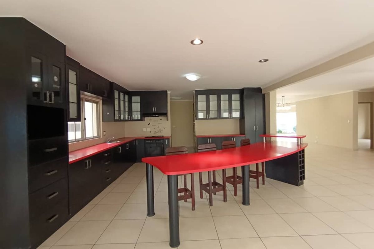Spacious kitchen featuring dark cabinetry, vibrant red countertops, a large integrated breakfast bar, and tiled flooring, offering ample storage and workspace.