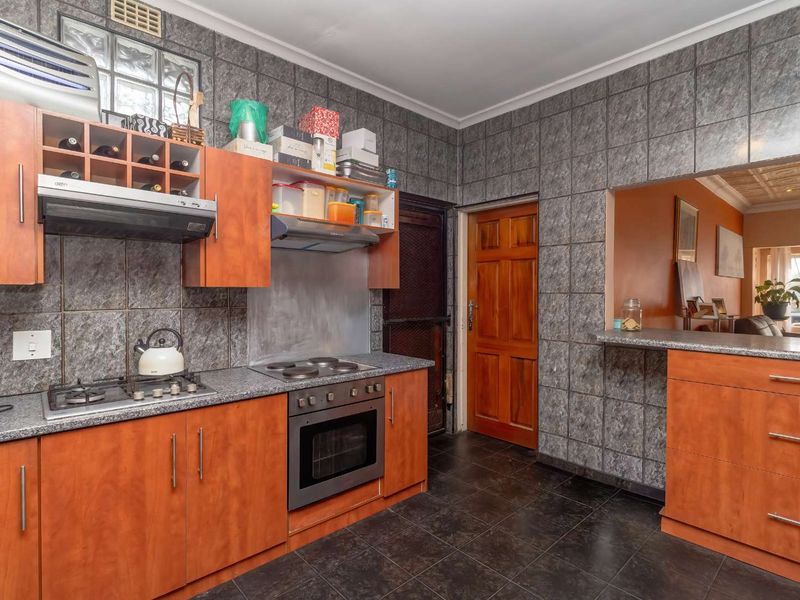 A functional kitchen featuring wooden cabinetry, granite countertops, a gas hob, an electric oven, and a breakfast bar opening into the living area.