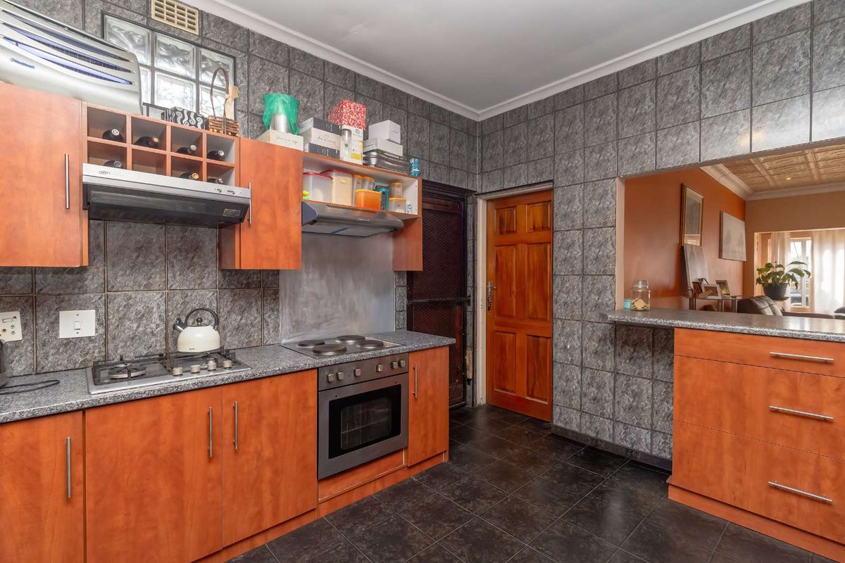 A functional kitchen featuring wooden cabinetry, granite countertops, a gas hob, an electric oven, and a breakfast bar opening into the living area.