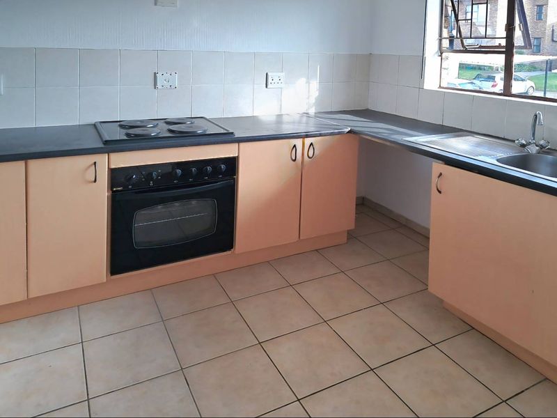 A functional kitchen featuring built-in oven, electric hob, stainless steel sink, and tiled backsplash with ample laminate cabinetry and ceramic floor tiles.