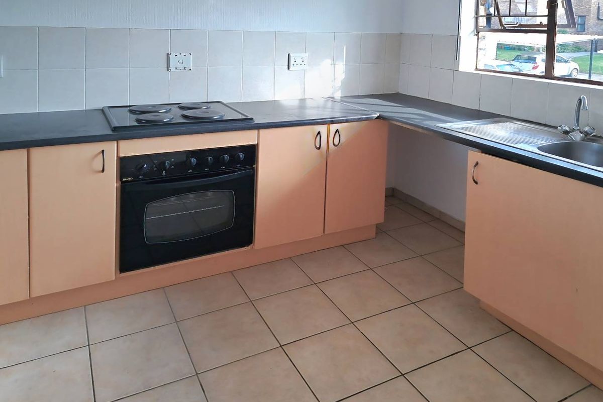A functional kitchen featuring built-in oven, electric hob, stainless steel sink, and tiled backsplash with ample laminate cabinetry and ceramic floor tiles.
