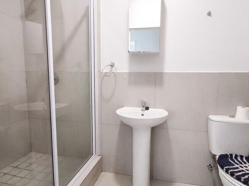 A functional bathroom featuring a pedestal washbasin, a glass-enclosed shower, and a standard toilet with neutral wall tiling.