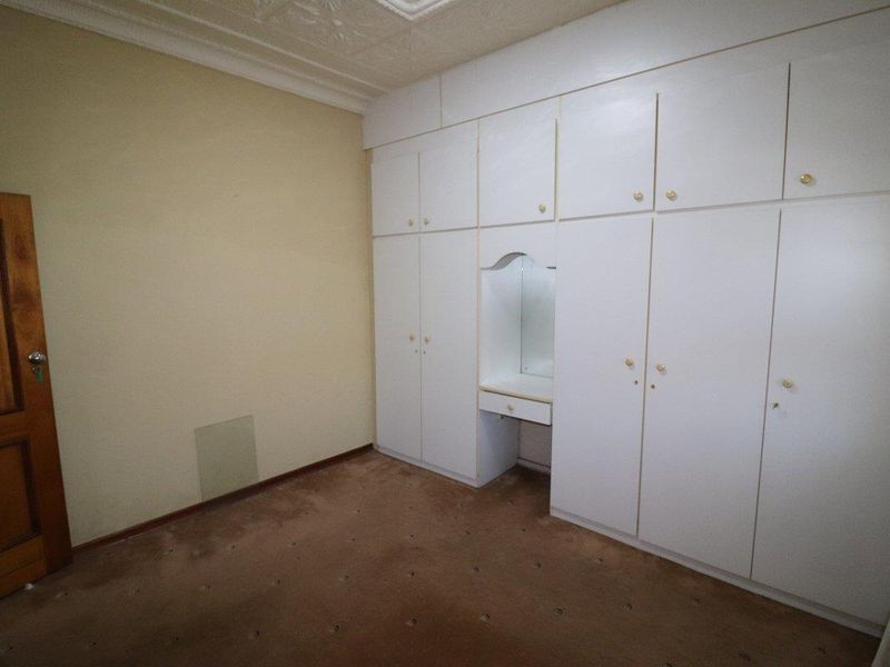 A vacant bedroom featuring extensive built-in white cabinetry with an integrated vanity unit, decorative ceiling cornice, and brown carpeting.