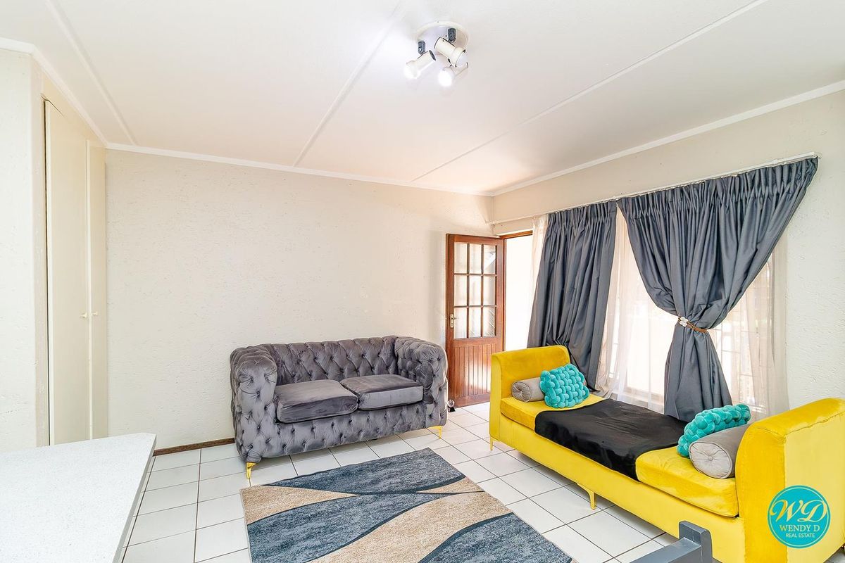 A bright living room featuring tiled flooring, a timber-framed door, and a ceiling-mounted spotlight fixture, offering a functional and well-lit space.