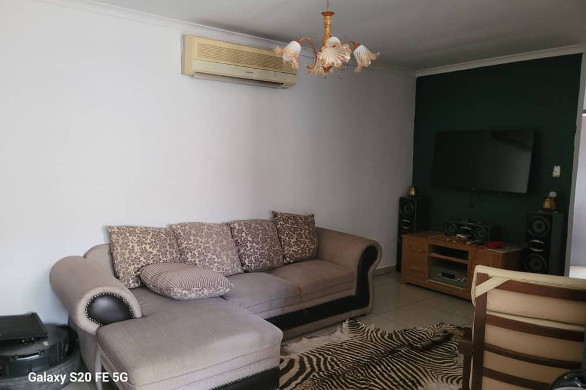 A living room featuring tiled flooring, a wall-mounted air conditioning unit, and a decorative chandelier.