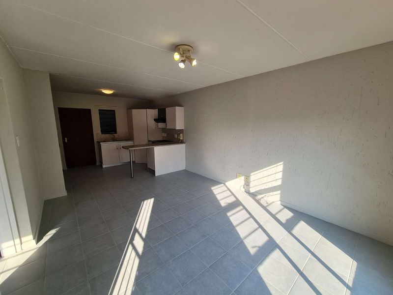 An open-plan living and kitchen area featuring tiled flooring, built-in cabinetry, and a functional kitchen layout in a vacant apartment setting.