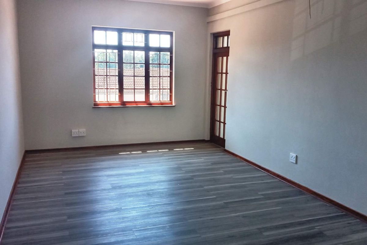 A bright, empty office space featuring modern laminate flooring, timber-framed windows, and a matching glass-paneled door, providing a clean and professional work environment.