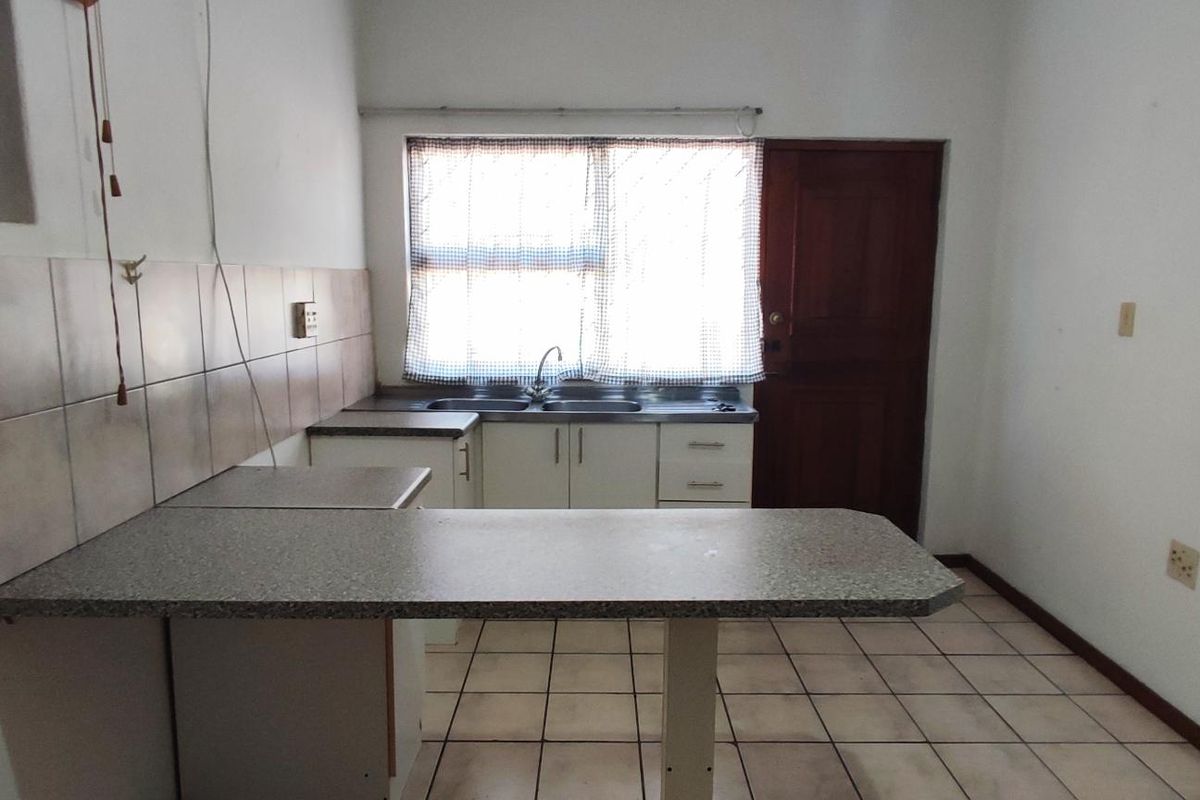 A functional, empty kitchen featuring tiled flooring, a breakfast bar, laminate countertops, and a stainless steel sink, ready for modernization.