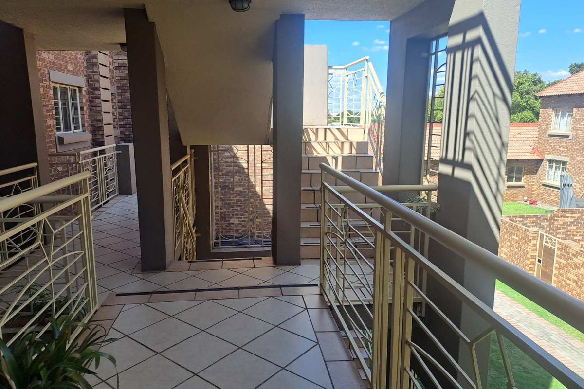 An outdoor stairwell and landing area featuring tiled flooring, metal safety railings, and concrete structural pillars within an apartment complex.