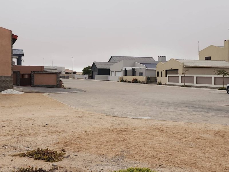 A view of the residential street showing paved road access and surrounding established boundary walls in a quiet neighborhood setting.