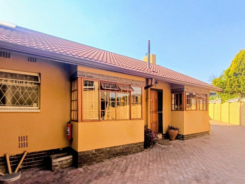 Rear exterior view of the house featuring a tiled roof, brick paved courtyard, and secure entrance with security gate.