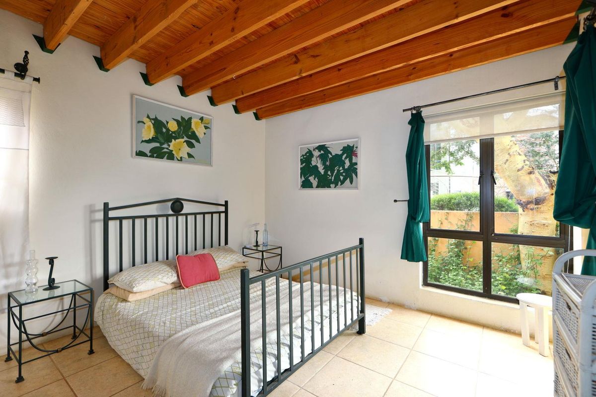 A bedroom featuring exposed timber ceiling beams, tiled flooring, and a large window overlooking the garden.