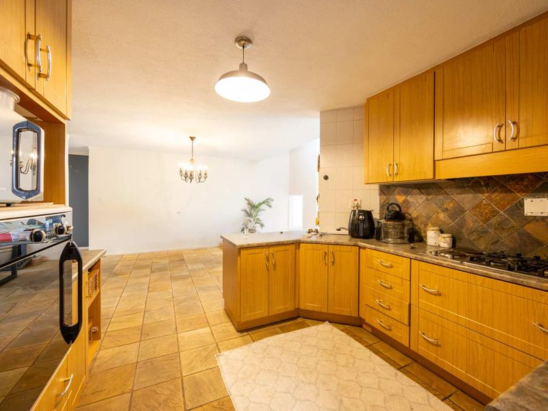 Open-plan kitchen and dining area featuring wooden cabinetry, gas hob, built-in oven, and durable stone tile flooring throughout the space.