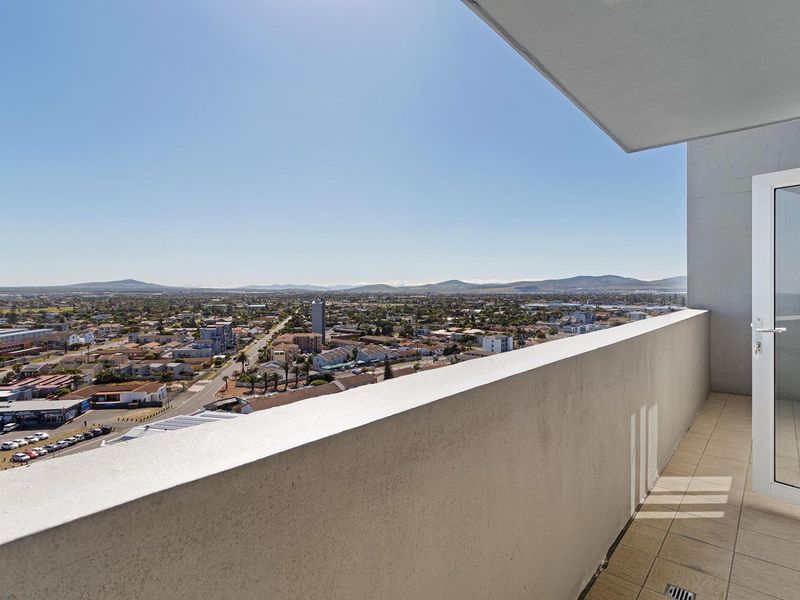 A spacious balcony featuring tiled flooring and a concrete balustrade, offering expansive panoramic views of the surrounding urban landscape.