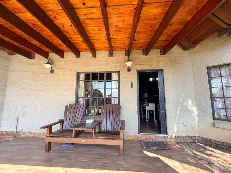 A covered patio area featuring a rustic exposed timber beam ceiling, tiled flooring, and steel-framed windows, providing a charming outdoor transition space.