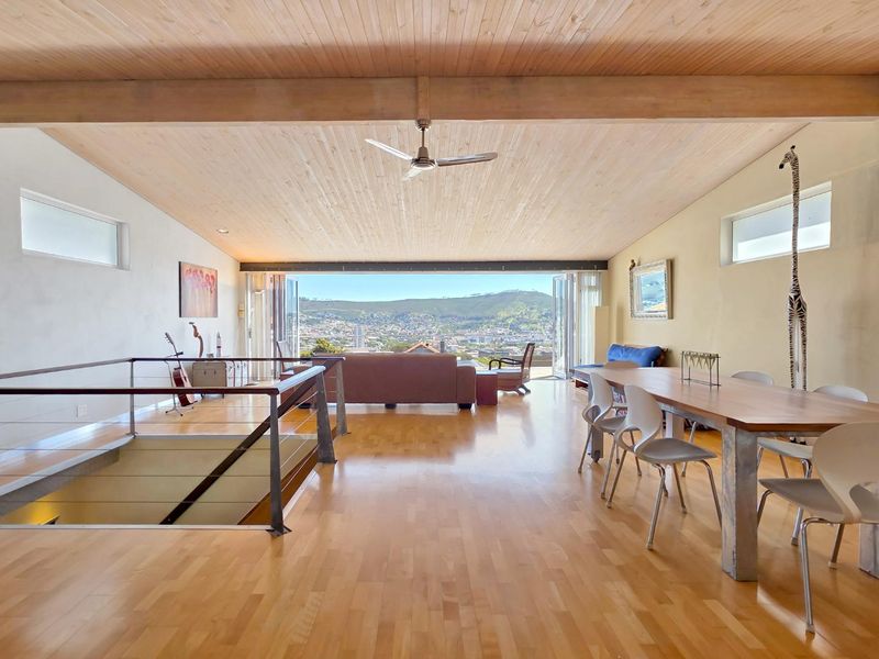 Spacious open-plan living and dining area featuring high timber ceilings, hardwood floors, and expansive folding glass doors opening to a scenic mountain view.